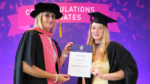Two people in graduation attire; one hands a certificate to the other
